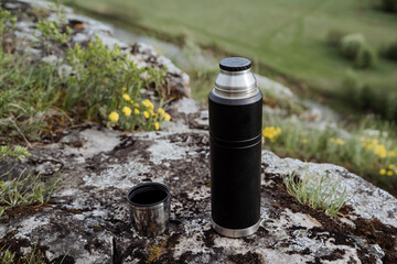 Drink tea in nature from a thermos, open lid, pour tea into a mug, hike in the mountains, camping in nature, tourist dishes, thermo bottle.