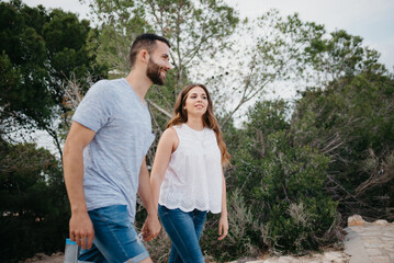Fototapeta premium A Hispanic man and brunette woman are walking in the park in Spain in the evening. A couple of tourists on a date at sunset in Valencia.