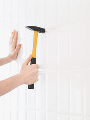 The hands of a young caucasian guy hammer a dowel into a drilled hole on a tiled wall