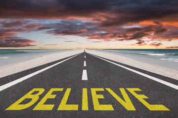 Believe text written on a highway at the beach with the sunset in the background for belief or faith concept.