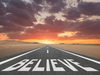 Believe text written on a highway at the beach with the sunset in the background for belief or faith concept.