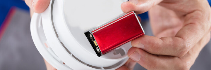Person's Hand Inserting Battery In Smoke Detector
