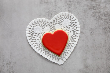 Backdrop with heart shaped sugar cookie with royal icing on top of a white doily with copy space.