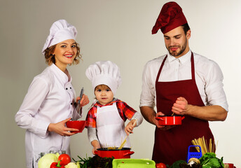 Happy parents teach little son cooking. Family with small child boy preparing food at kitchen.