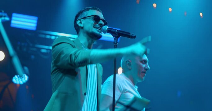 Live performance singer man on glasses, dancing on concert musician stage with lights