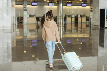Traveling with children. cute teenage girl walking together with travel suitcase in airport. cute child girl goes on trip abroad on weekends. back view