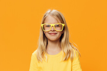 Fototapeta premium portrait of a cute beautiful school-age girl in yellow glasses for vision on a yellow background, pleasantly smiling looking at the camera
