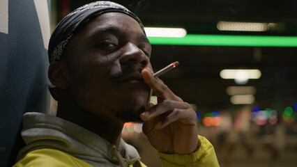 African american man smokes cigarette inhaling harmful smoke with nicotine while standing near wall...