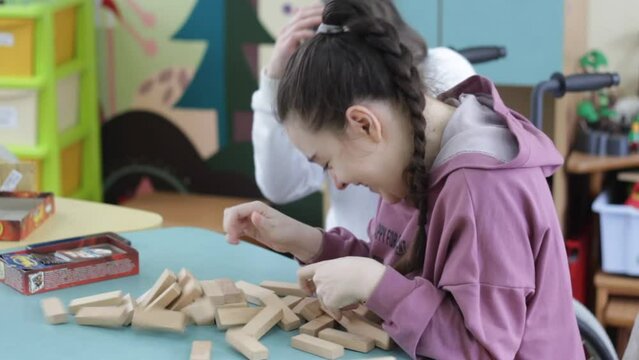 two girls with disabilities are playing a board game sitting at a large table. Rehabilitation of people with disabilities.