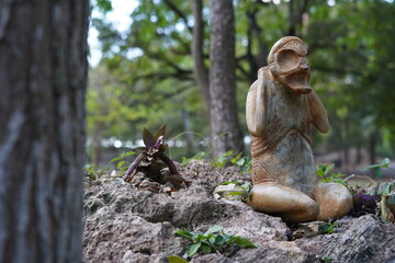 Taino Antique Stone Cemi Idol God Figure standing on rocks on the ground next to a tree, close up....