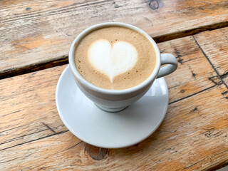 A cup of coffee latte On a wooden table. A mug of flat white coffee on a wooden background. Coffee art. Heart flower shape latte art. Copy space