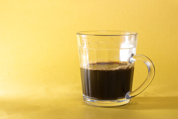 Glass cup with black coffee isolated yellow background