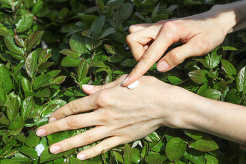 Applying of the moisturizing skincare hand cream on woman's palm among the green leaves