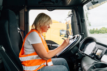 Mature woman truck driver steering wheel inside lorry cabin. Happy middle age female trucker...
