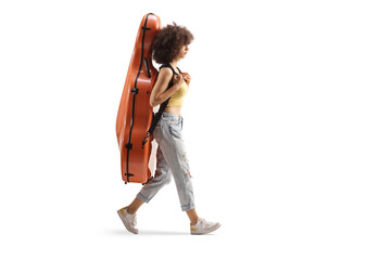 Full length profile shot of a young woman walking and carrying a contrabass in a case on her back