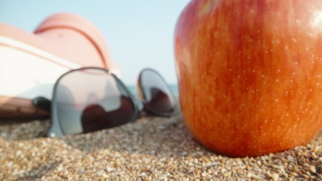 Things on the beach by the sea. Through pink flip flops and sunglasses and a red apple. Dolly slider extreme close-up. Laowa Probe.