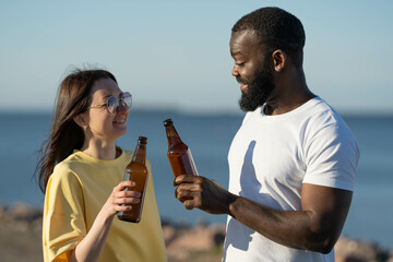 Diverse couple toasting and drinking beer from bottles. Seaside vacation.