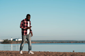 African american young man in plaid red shirt walking by sea.