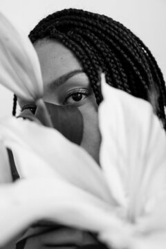black and white portrait of a girl whose hair is braided, looking through a large lily flower, because of which only her eye is visible