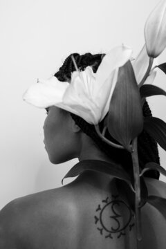 black and white photo of a girl whose hair is braided with a tattoo on her back and a lily flower along the spine