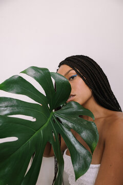 beautiful dark-skinned girl in a white strapless pope on a white background with a large green leaf of a plant