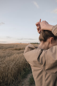 girl in a beige coat on a walk in a wheat field straightens hair with hands