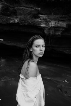 portrait of a girl in a light shirt looking at the camera on a black sandy beach