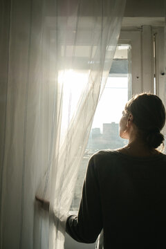 girl with gathered hair near the window with early sunlight pushing back the tulle