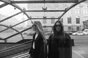 black and white portrait of two girls walking in the city at the entrance to the subway