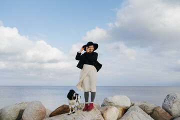 Woman with dog standing on the big stones near the sea