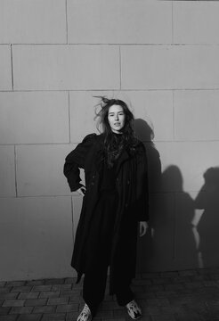 black and white photo of a girl in a long raincoat whose hair flutters in the wind in the city