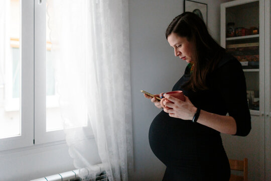 Pregnant woman in black checking phone at home