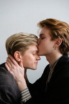 portrait of two guys in love who in a light studio sitting opposite each other kiss and gently hug each other