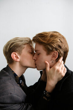 portrait of two guys in love who in a light studio sitting opposite each other kiss and gently hug each other