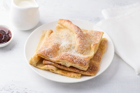 A plate of traditional finnish or danish pancakes pannukakku sprinkled with powdered sugar with sour cream and jam on a light background. Delicious vegetarian homemade breakfast