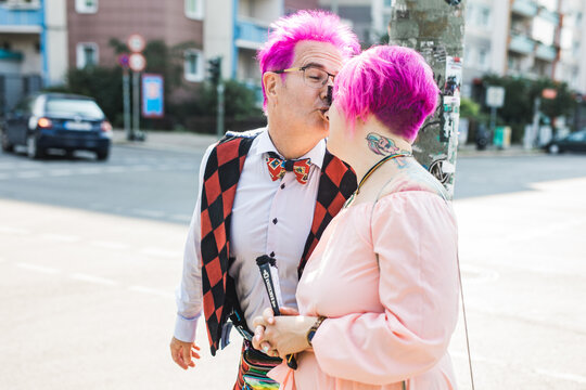 Man and woman with acid pink hair starring a kiss outside