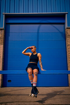 Non binary model at a blue door covering their face and wearing skates