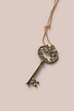 Bronze ornate key with golden chain on beige background