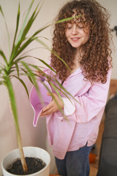young curly woman caring for home plants