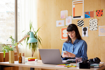 Woman using laptop at desk with laptop in creative room