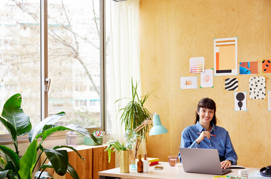 Cheerful woman using laptop in creative workplace