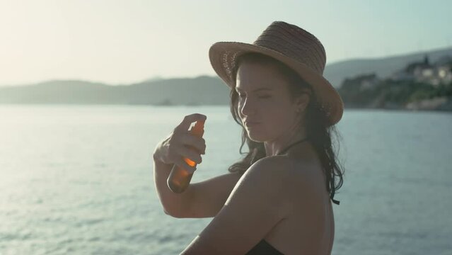Woman rubs sun protective cream on body slow motion video. Sunscreen is applied by a girl sunbathing by the ocean on the beach.