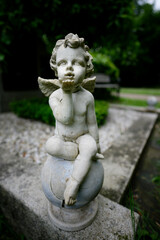 Fototapeta na wymiar damaged small angel figure sends love greetings sitting on a stone ball at a grave