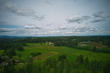 An aerial view of a rural landscape of green fields, trees, and a cloudy sky.
