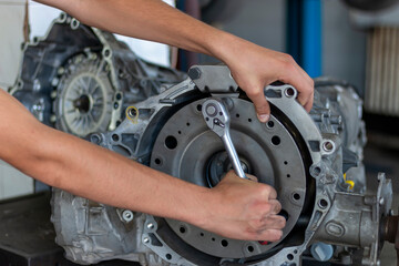 A close-up of teenager repairman repairing a gearbox of a used car in an auto repair shop. Car repair and maintenance.