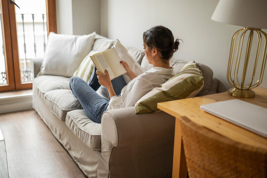 Caucasian young woman reading a book at home