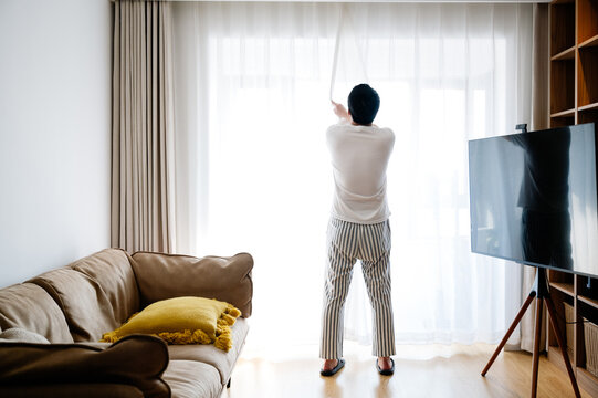 Young man opening the curtain in the morning