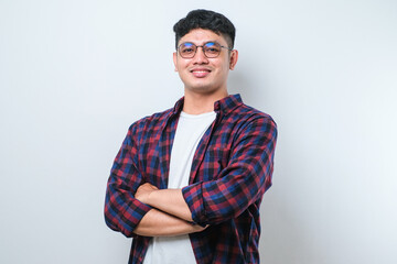 Portrait of young handsome Asian man wearing casual shirt and glasses standing with arms crossed and smiling at camera