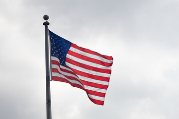 American flag blowing in the wind on a flagpole with a cloudy sky in the background