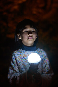 Closeup cute little chinese girl playing with a glowing light bulb